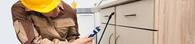 Roach exterminator applying treatment under kitchen cabinets in Hialeah, FL