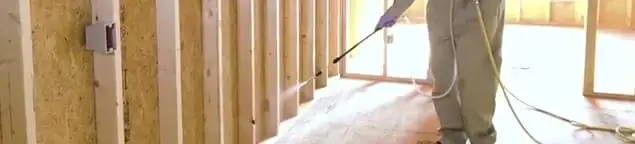 Termite treatment technician applying spray along framing and unfinished walls in Hialeah, FL